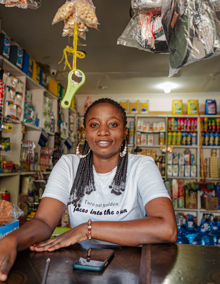 A shop owner behind the counter of her duka, mobile phone beside her